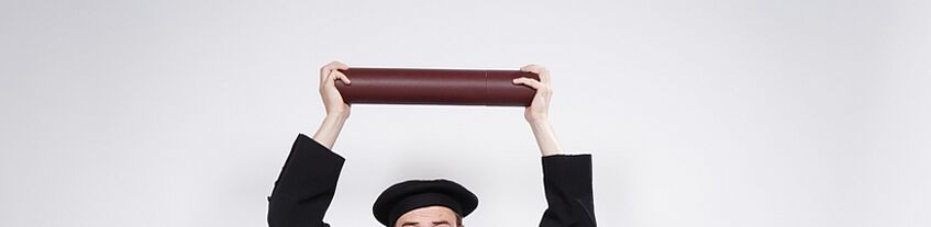 Person im Talar hält Diplom mit beiden Händen in die Höhe