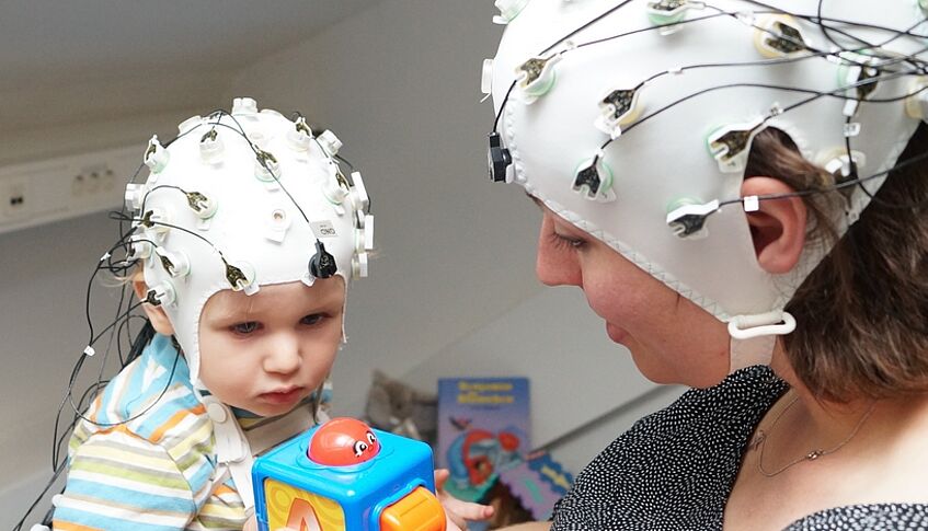 Frau und Kind mit EEG-Kappe in Spielsituation