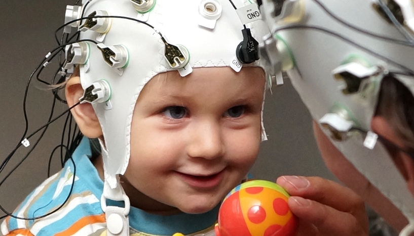 Erwachsene Person und Kind in Spielsituation mit EEG-Kappen